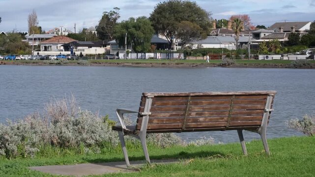 A waterfront park bench sits on a grassy foreshore reserve overlooking residential street of Williamstown with upscale houses, Melbourne Australia. Concept of bayside suburban living, outdoor leisure