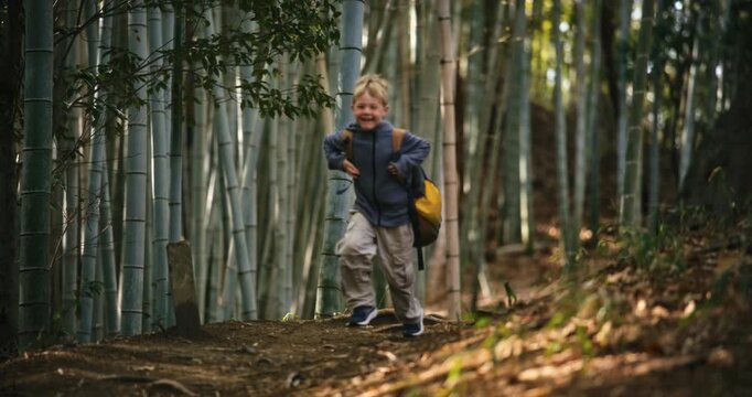 Joyful kid with backpack running through bamboo grove - slow motion shot