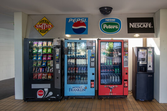 A row of vending machines dispensing snacks, soft drinks and hot beverages at a public venue in Melbourne Australia. Brand signage above the machines includes Pepsi, Peters Ice Cream, Smith's Crisps.