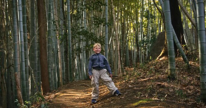 Boy posing on dirt road surrounded by tall bamboo trees - wide shot