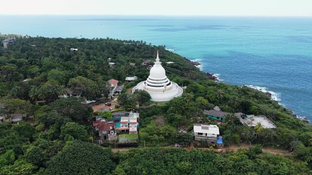 Aerial view of the white Japanese Peace Pagoda surrounded by dense tropical forest and the blue Indian Ocean in Unawatuna, Southern Province, Sri Lanka.