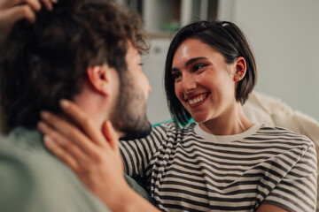 Fototapeta premium Young woman smiling at her partner while gently touching his neck, sharing a loving moment at home. Intimacy and connection
