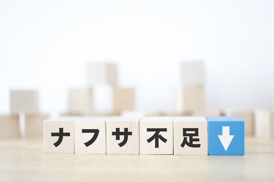ナフサ不足。石油由来製品の供給不足。下矢印。木製ブロック。白背景