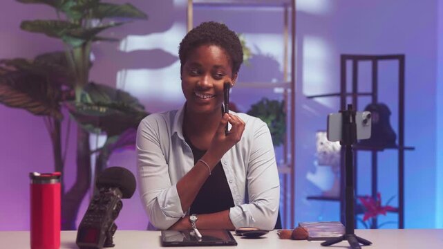Young African woman applying makeup while recording a beauty vlog on her smartphone