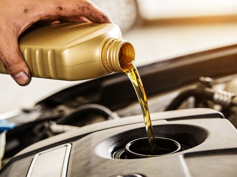 A close-up shot of a mechanic's dirty hand pouring fresh golden engine oil into a car engine.