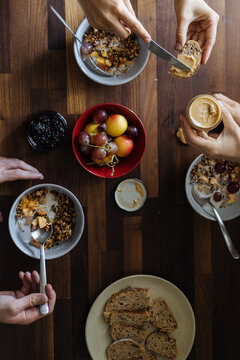 Crop hands spreading peanut butter and taking muesli