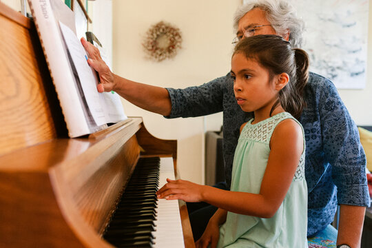 Grandmother and granddaughter play piano with sheet music at home