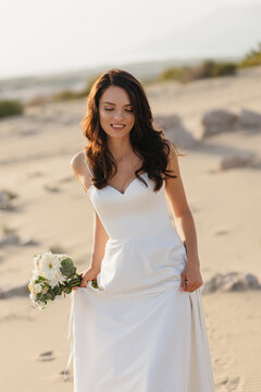 Happy bride holding bouquet walking on desert sand