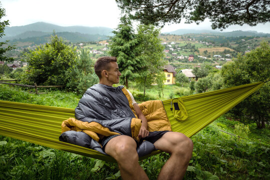 Happy man relaxing in a hammock among trees with a scenic view.