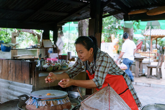 Woman cooking steamed eggs on steamer inside Thai heritage restaurant