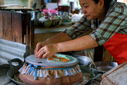 Woman cooking steamed eggs on steamer inside Thai heritage restaurant