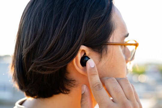 Young man wearing glasses inserting wireless earbud into ear
