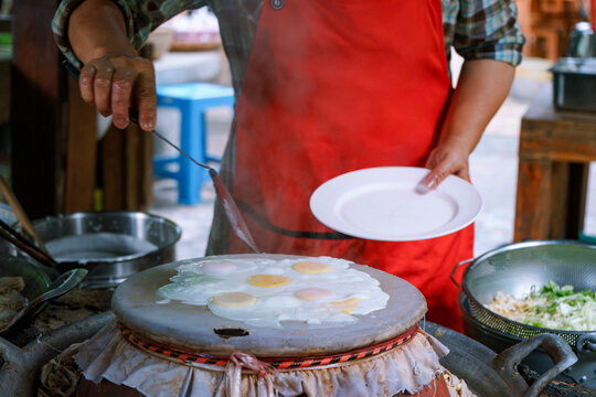Woman cooking steamed eggs on steamer inside Thai heritage restaurant