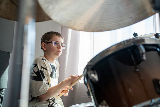 Young Boy Plays Drums in Sunny Room During Afternoon