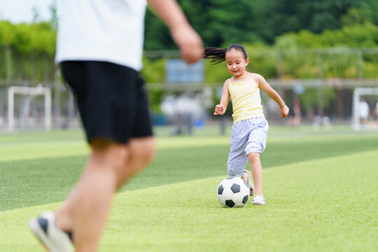 Little Girl Practicing Soccer Skills on Grass Field in Sunny Day