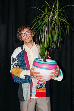 Young man holds large pot with plant in a studio