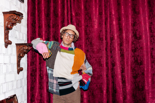 Man stands in front of red curtain wearing a colorful sweater