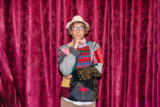 Man stands in front of red curtain wearing a colorful sweater