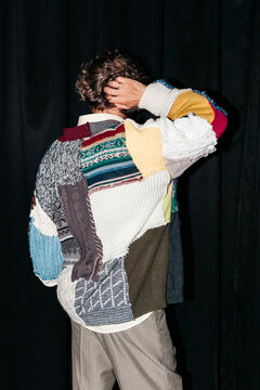 Man with curly hair wearing a colorful patchwork sweater