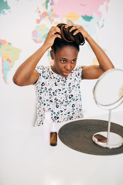 Woman with natural acne skin braiding her hair in a bun at home