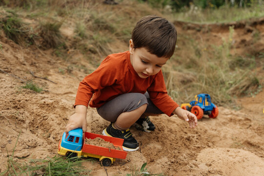 Child playing with toy trucks in sand outdoors