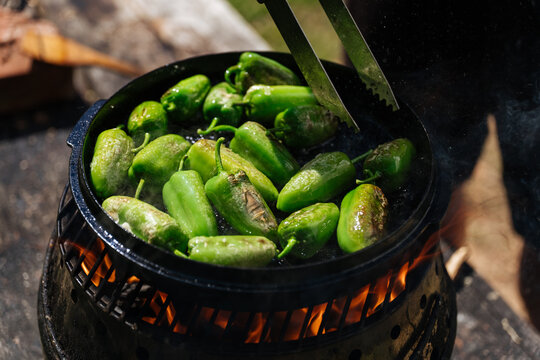 Green peppers roasting in cast iron pan over open flame