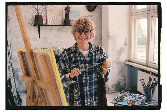 Artist stands in studio with paintbrush smiling