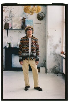 Man stands in a bright room with a patterned jacket and beige pants