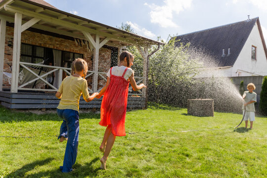 A boy waters his sister with a hose