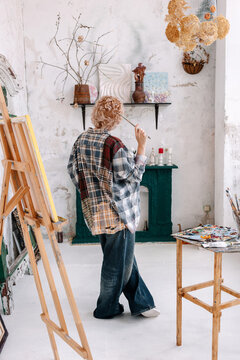 Artist works in a studio with paint, easel, and creative tools