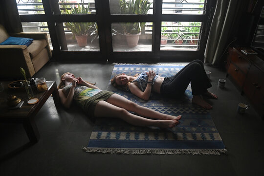 two teenage girls lie on a rug in their living room