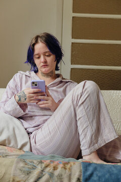 Young person wearing pajamas checking smartphone in the couch