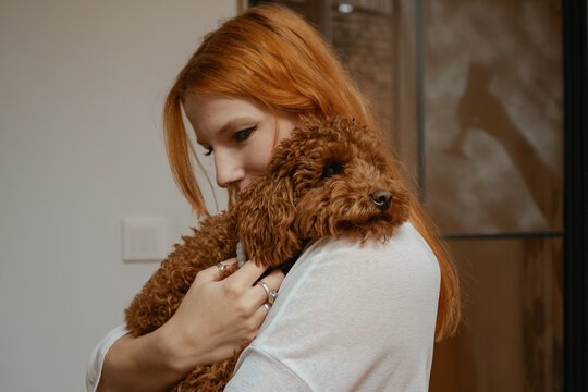 Woman holds a poodle close in a warm indoor setting