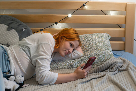 Young woman relaxes on bed while using phone in cozy room