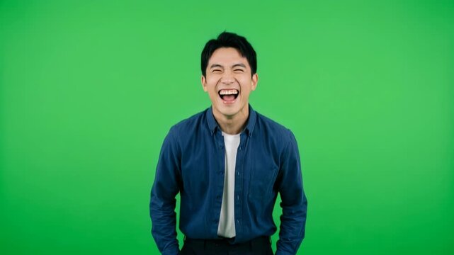 Cheerful Young Asian Man Laughing Out Loud on Green Screen Background for Joyful Content, Comedy Video, and Creative Advertising Projects