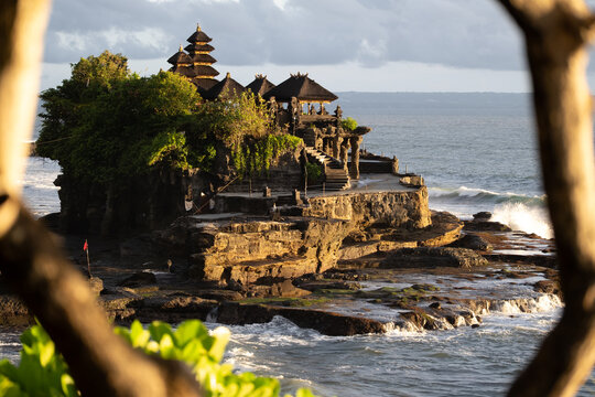 Temple on coastal rock formation framed by tree branches