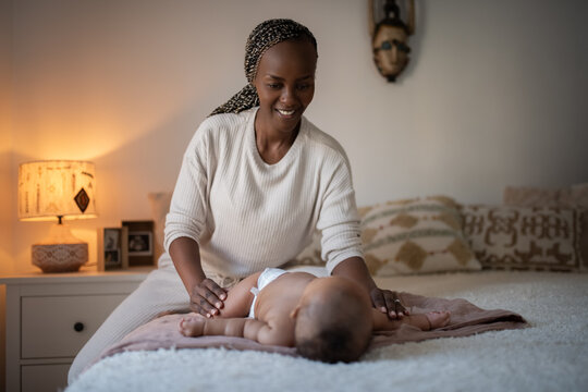 Smiling mother stretching her newborn baby body at home 