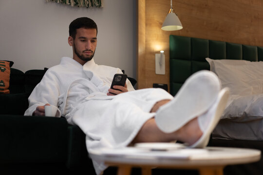 Relaxed Guest in Bathrobe Checking Phone on Sofa