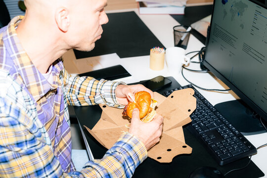 Man Eats Sandwich While Working at Desk With Computer
