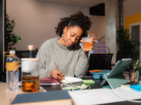 Woman taking notes while holding cup of tea 
