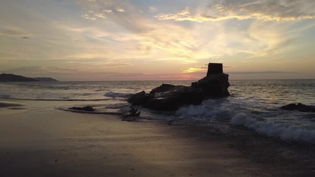 Low drone shot of ocean waves crashing on rock at Santa Marianita beach, Ecuador, at sunset.