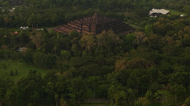 Aerial view of Borobudur Temple nestled within dense tropical forest and lush greenery in Kecamatan Borobudur, Jawa Tengah, Indonesia.