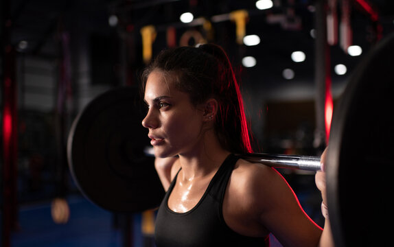 Sweaty woman exercising with barbell in gym