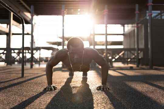 Black man in earphones pushing up on sport ground