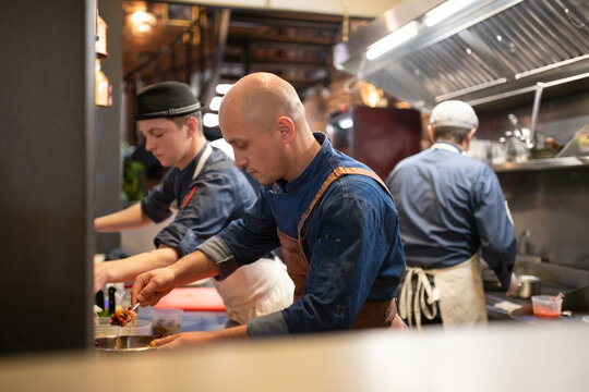 Bald chef preparing pasta near team in kitchen