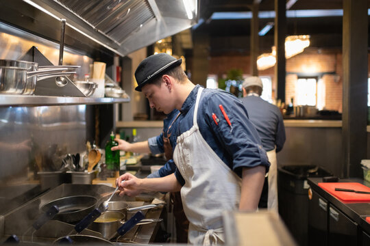 Young cook checking pasta in saucepan