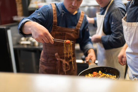 Cropped chef serving pasta near colleagues