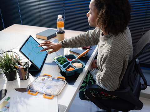 Woman reviewing project on computer while eating linch 