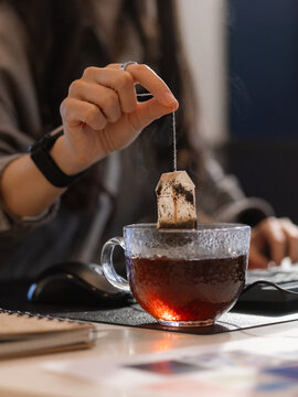 Woman brewing tea in glass mug at workspace 