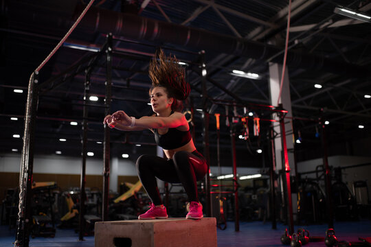 Powerful sportswoman jumping on gym box